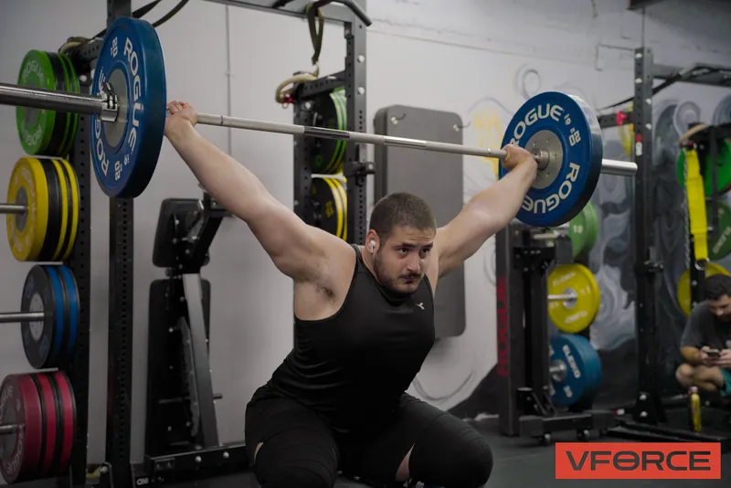 מתאמן בתחתית תרגיל עם מוט מעל הראש